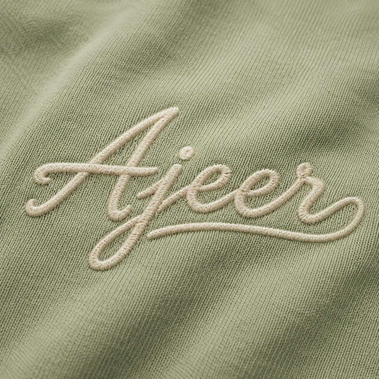 Close-up of custom logo embroidery on hoodie fabric featuring cream embroidered AJEER branding on light green material