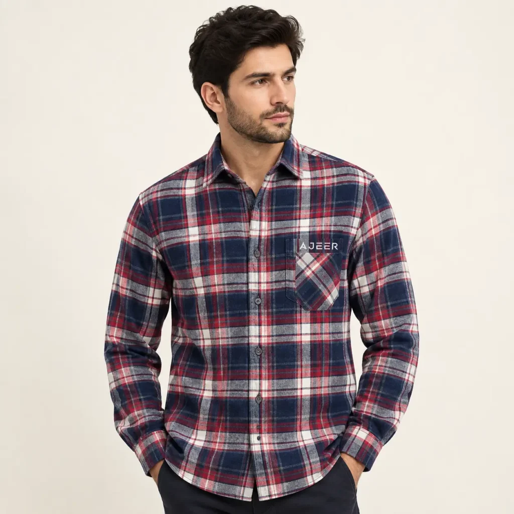 One adult male fashion model wearing a traditional classic button-front flannel shirt. The shirt has a regular, balanced fit, long sleeves, traditional pointed collar, full button placket, buttoned cuffs, and a clean chest pocket. Plaid pattern with a sophisticated combination of navy, red, white, and subtle neutral tones with small, AJEER logo.
