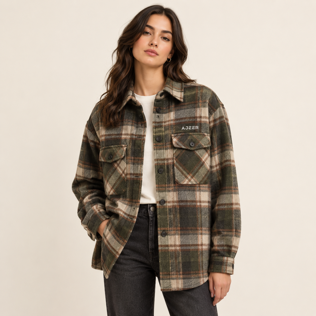 one adult female fashion model wearing a modern flannel overshirt designed as a shirt-jacket style layer. The garment should have a relaxed but structured fit, slightly heavier appearance than a traditional shirt, a full button or snap-front closure, substantial collar, long sleeves, buttoned cuffs, and practical chest pockets. Has small, subtle AJEER INDUSTRIES logo. 